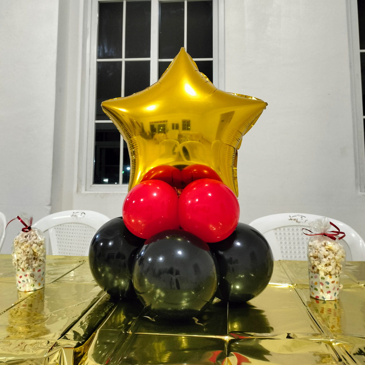 Centro de mesa para fiesta montado sobre mesa dorada con arreglos de globos y recuerdos.